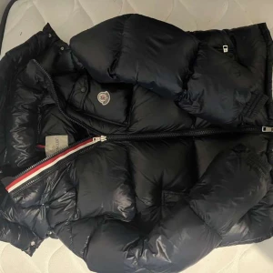 Moncler montbelliard mörk blå - Säljer en Moncler med huva och dragkedja. Jackan har en klassisk pufferstil och Moncler-logga på bröstet. Perfekt för kyliga dagar och riktigt snygg till streetwear.