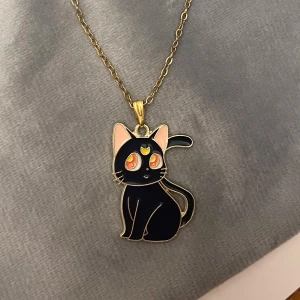 Sailor Moon Luna Halsband guld imitation - Ett gulligt halsband med katten Luna från Sailor Moon 🌙 🐈‍⬛💕 Kedjan är i guldimitation och justerbar 40-45 cm. Berlocken är ca 3 x 2 cm. Perfekt present för ett Sailor Moon-fan! 