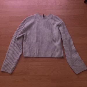Grå ribbad stickad tröja från H&M - Säljer en grå ribbad stickad tröja från H&M. Tröjan har en croppad passform och långa ärmar. Perfekt för lager-på-lager och enkel att matcha med olika outfits.