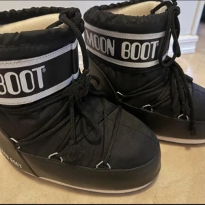 Svarta Moon Boots med snörning - Svarta Moon Boots med vit logga och snörning runt skaftet. Perfekta för vintern med sin ikoniska design och syntetmaterial som håller fötterna torra och varma. Endast använda ett par gånger. Se bilder, inget synligt men reserverar mig för missar.  Nypris ca 1500kr. 