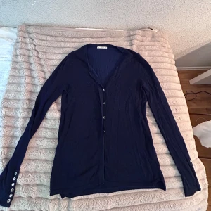 Mörkblå kofta från Zara med knappar - Mörkblå tunnstickad kofta från Zara i storlek S. Långärmad modell med silverfärgade knappar framtill och längs ärmsluten. Enkel och stilren design som är lätt att matcha. Perfekt för lager-på-lager och chillare dagar.