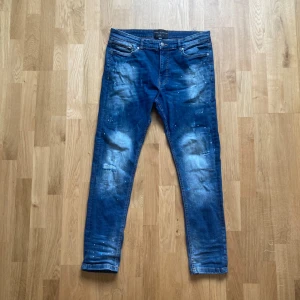 Blå jeans från Supply & Demand - Säljer ett par blå jeans från Supply & Demand med slitna detaljer och färgstänk. Storlek 34 width och Length.