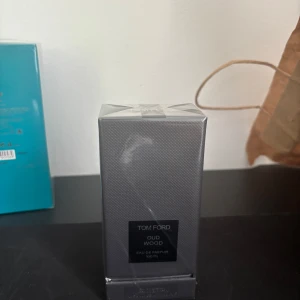 Tom Ford Oud Wood Eau de Parfum 100 ml - Lyxig parfym från Tom Ford i doften Oud Wood. Flaskan rymmer 100 ml och kommer i en elegant, mörkgrå förpackning med diskret mönster. Perfekt för dig som gillar exklusiva och träiga dofter.