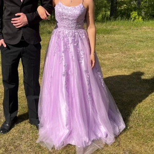 Ljuslila balklänning med broderier - Drömmig ljuslila långklänning med tunna axelband, vacker snörning i ryggen och broderade blommor över hela klänningen. Kjolen är i flera lager tyll som ger en riktigt prinsessig känsla. Perfekt till balen. Den har ett litet kort släp som lägger sig fint på marken när man går☺️☺️ Den passar många olika storlekar eftersom det är snörning i ryggen så den passar många🤗
