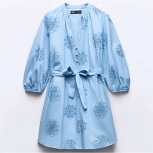 Ljusblå klänning med broderade blommor från Zara - Supersöt ljusblå klänning från Zara med broderade blommor och knytband i midjan. Klänningen har trekvartsärmar med resår och en avslappnad passform. Perfekt för vår och sommar!