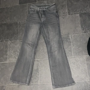 Grå bootcut jeans med broderade fickor - Säljer ett par grå bootcut jeans med snyggt vitt broderi på bakfickorna. Jeansen är väldig tight i midjan, så skulle egentligen säga att dessa jeans är i storlek XS pågrund av att de är så tight vid midjan. Dessa jeans är tillverkade i en mjuk bomullsblandning med lite stretch. Perfekta för dig som vill ha något unikt i garderoben!