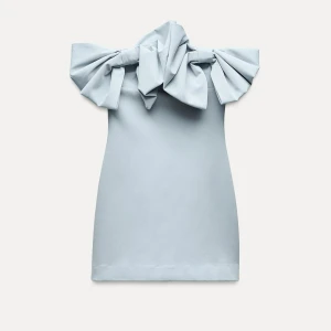Ljusblå kort klänning med stora rosetter - Superfin ljusblå kort klänning från Zara med stora statement-rosetter över axlarna. Klänningen är axelbandslös och har en rak, enkel passform som ger en cool och modern vibe. Perfekt för dig som vill sticka ut med en unik detalj! Helt oanvänd i stolek xs, 