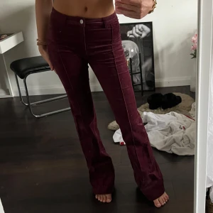 Vinröda manchesterbyxor med bootcut - Säljer ett par vinröda manchesterbyxor med bootcut i mod waist Byxorna har klassisk femficksdesign, knäppning med dragkedja och knapp framtill. Snygg passform som sitter tight upptill och släpper ut vid benen.