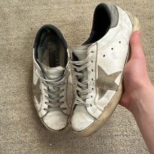 Golden Goose skor - Tja! Säljer nu dessa feta golden goose skor! De är i bra skick, men saknar box osv. Därför det låga priset! Storleken är 40, men kan passa upp till 41. Vid hälen har det gått bort lite tyg, men känns inte alls. Sulan är lite trasiga där bak, men går enkelt att fixa och märks inte. Utöver det så är skicket 8/10 skulle jag säga. Nypris: 5999kr❌‼️ Mitt pris: 1699kr✅ Skriv ifall du har frågor och pris kan diskuteras!🙌🤝