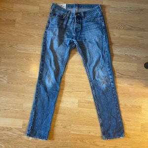 Blå jeans från Hollister - Säljer ett par klassiska blå jeans från Hollister med raka ben och normal passform. Jeansen har fyra fickor, knappgylf och råa benslut för en avslappnad look. Perfekta till vardags och lätta att matcha med olika stilar.