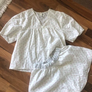 Vit blommig pyjamas ❣️🌸💕🎀 - Söt vit pyjamas med små rosa blommor och v-ringning med spetsdetaljer. Blusen har korta ärmar och har en luftig passform💕 Shortsen har ett elastiskt midjeband och är i samma underbara material som toppen🎀🌸💕 