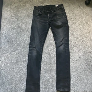 Dondup George - Säljer ett par svarta Dondup George 30W med lätt slitning vid knäna och klassiska fem fickor. Jeansen har dragkedja och knapp i midjan och är i stretchigt material för en bekväm passform.