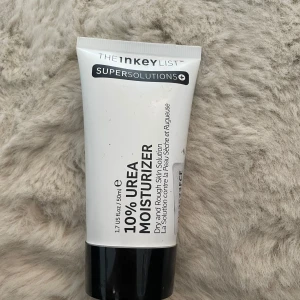 The Inkey List 10% Urea Moisturizer - Fuktkräm från The Inkey List med 10% urea, perfekt för torr och sträv hud. Kommer i en vit tub med svart lock, 50 ml. Lätt formula som återfuktar och mjukgör huden snabbt. Tuben är tillverkad av återvunnen plast.