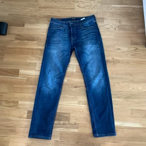 Blå jeansbyxor från Jack & Jones 30/32 - Snygga blå jeansbyxor från Jack & Jones i klassisk straight fit. Jeansen har fem fickor, normal midja och coola slitningar framtill för en avslappnad look. Perfekta till sneakers och hoodie för en chill stil. 
