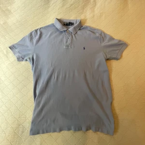 Ljusblå piké från Ralph Lauren - Snygg ljusblå pikétröja från Ralph Lauren. Klassisk krage, korta ärmar och broderad logga på bröstet. Perfekt för en clean och avslappnad stil, funkar lika bra till jeans som shorts.