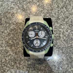 Omega x Swatch Speedmaster Mission on Earth - Säljer en Omega x Swatch Speedmaster Mission on Earth med mintgrönt boett, svart urtavla och vita detaljer. Klockan har vit silikonrem, tachymeter och tre subdials. Baksidan har en bild på jorden och texten 'Mission on Earth'. Riktigt snygg och unik klocka!