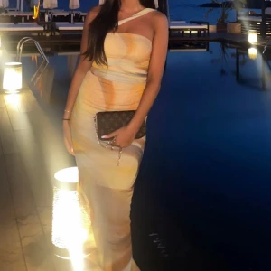 Lång pastellfärgad sett med band runt halsen - Supersnyggt sett i pastelliga toner av beige, gult och vitt. Settet har en tight passform, är ärmlös och har ett unikt asymmetriskt axelband. Perfekt för sommarkvällar och ger en elegant siluett. TOPP och KJOL