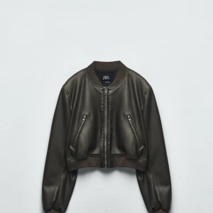 Svart bomberjacka i skinnimitation från Zara - Snygg svart bomberjacka från Zara i skinnimitation. Jackan har dragkedja framtill, två snedställda fickor med dragkedja och ribbade muddar vid ärmslut, krage och nederkant. Nästan alldrig använd