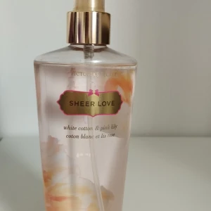 Victoria's Secret Sheer Love body mist 250ml - Fräsch body mist från Victoria's Secret i doften Sheer Love med noter av vit bomull och rosa lilja. Perfekta clean girl doften. Flaskan är transparent med guld- och rosa detaljer och rymmer 250 ml. Perfekt för dig som gillar blommiga och lätta dofter.