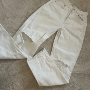 Vita jeans med slitna knän Gina Tricot - Vita jeans från Gina Tricot med raka ben och slitna detaljer vid båda knäna. Klassisk femficksmodell i kraftig denim med snygga silverfärgade knappar.  