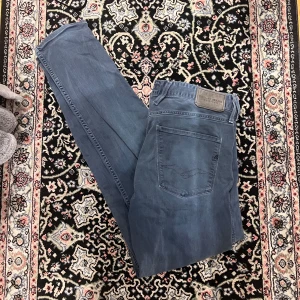 Replay anbass mörkblå 33/34 - Snygga blå jeansbyxor från Replay med klassisk femficksdesign och logotyp-patch bak i midjan. Byxorna har raka ben och normal passform, perfekta för en avslappnad stil. Tidlös modell som funkar till mycket.