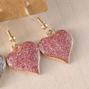 Glittriga hjärtformade örhängen - Säljer ett par örhängen med hjärtformade hängen i rosa och silverglittrigt material. Perfekta för att ge din outfit lite extra bling! Hängena sitter på guldfärgade krokar.