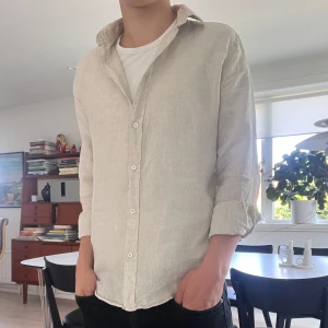 Beige linneskjorta  - Säljer en stilren beige skjorta i linne från Zara. Skjortan har klassisk krage, knäppning framtill och långa ärmar. Perfekt för dig som gillar en avslappnad men ändå snygg look. Finns inga täcken på användning och är i jättebra skick. Använd endast 2 gånger.