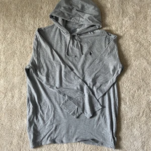 Grå hoodie från Polo Ralph Lauren - Säljer en stilren grå hoodie från Polo Ralph Lauren med klassisk huva och dragsko. Tröjan har lång ärm och den ikoniska broderade loggan på bröstet. Perfekt för en avslappnad och snygg look.