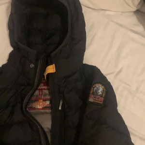 Svart dunjacka Parajumpers S - Säljer en svart dunjacka från Parajumpers i storlek S. Jackan har huva, klassisk patch på ärmen och cool gul detalj vid dragkedjan. Insidan är grå och jackan är quiltad för extra värme. Perfekt för kalla dagar och riktigt snygg streetstil.