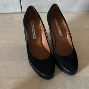 Svarta wedgespumps i mocka och skinn - Snygga svarta pumps från & Other Stories med kilklack. Ovandel i mocka och detaljer i skinn, spetsig tå och hög klack. Perfekta för dig som vill ha en stilren och edgy look med extra höjd.