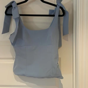 Ljusblå linnetopp med knyt från Zara - Supersöt ljusblå linnetopp från Zara med breda axelband som knyts i stora rosetter. Toppen har en rak, något figurnära passform och är perfekt för varma dagar. Stilren och enkel design som ändå sticker ut med sina knytband.