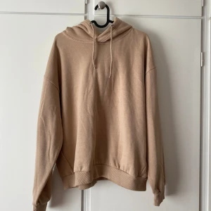 Beige hoodie - Säljer en oanvänd stilren beige hoodie med huva och snörning. Tröjan har en loose passform och är tillverkad i mjuk bomullsmix. Perfekt för chill dagar eller när du vill ha en enkel och clean look. 