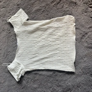 Vit ribbad topp från 157, S - Säljer en vit ribbad topp från 157 i storlek S. Toppen har korta ärmar och är tillverkad i ett stretchigt material med vågig struktur. Perfekt att styla med jeans eller kjol för en fräsch look. 