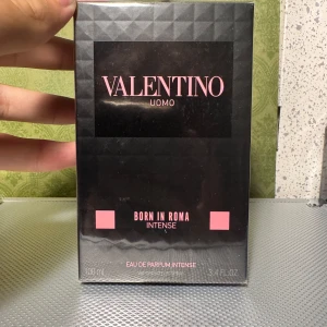 Valentino Uomo Born In Roma Intense 100ml - Valentino Uomo Born In Roma Intense är en eau de parfum i en snygg svart kartong med rosa detaljer. Flaskan rymmer 100 ml och doften är intensiv och modern. Förpackningen har en lyxig känsla med geometriskt mönster och tydlig logga framtill.