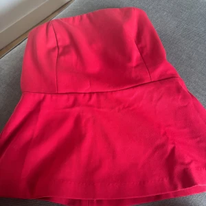 Röd tub/pepblum topp från hm - Snygg röd festtopp från H&M i storlek 38. Tippen har en figurnära passform upptill, smockad rygg och utsvängd nederdel. Perfekt att klä upp och ned🌹