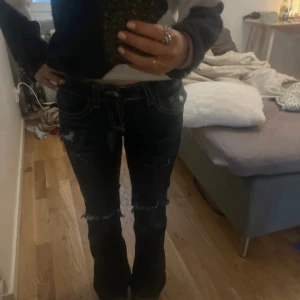 Mörka bootcut jeans med slitningar - Säljer ett par mörkblå bootcut jeans med snygga slitningar och råa kanter vid knäna. Jeansen har kontrastsömmar och klassiska fickor både fram och bak. Perfekta för dig som gillar en lite edgy och avslappnad stil.