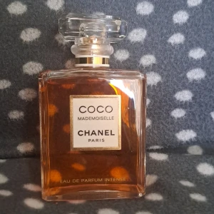 Chanel Coco Mademoiselle EdP Intense 100ml - Chanel Coco Mademoiselle Eau de Parfum Intense i elegant, fyrkantig glasflaska med guld- och vit etikett. Parfymen har en varm bärnstensfärgad vätska och kommer i en stilren vit kartong med guldiga detaljer. Flaskan har en lyxig, transparent kork.