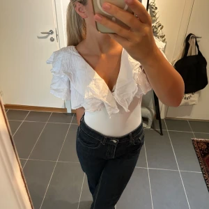 Zara volangbody - Supersöt vit body med djup v-ringning och stora volanger över axlar och bröst. Luftigt tyg som ger en romantisk vibe och passar perfekt till jeans eller kjol. Bodyn är ärmlös och har en feminin, flowy look som verkligen sticker ut.
