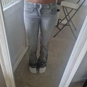 Grå bootcut jeans med låg midja - Säljer ett par grå jeans med snygg tvätt och låg midja. Modellen har bootcut-ben och klassiska fem fickor. Jeansen är i stretchigt denim som sitter skönt och ger en avslappnad vibe.