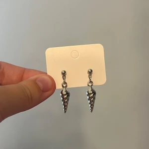 Silvriga snäckformade örhängen - Jag gör egna smycken. Ett par coola silvriga handgjorda örhängen med snäckformad design. Hängande modell med spiralformade detaljer som ger en unik och trendig look. Perfekta för dig som vill sticka ut lite extra med dina accessoarer.