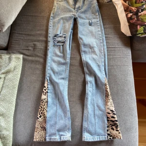 Jeans med leoparddetaljer - Unika ljusblå bootcut jeans med leopardmönstrade kilar längst ner på benen. Jeansen har klassisk femficksdesign och är tillverkade i bomull. Perfekt för dig som vill sticka ut med en cool och trendig look. Två slitningar på fickorna på baksidan (sista bilden) men inget som förstör funktionen. 