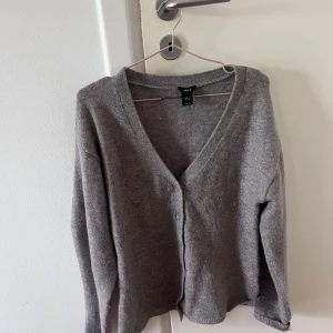 Grå kofta från Lindex med v-ringning - Mysig grå kofta från Lindex i storlek M. Koftan har v-ringad hals och är i nyskick men saknar prislapp. Nypriset för koftan var 400kr men säljer för 175