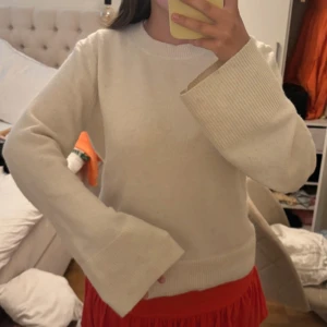 Beige stickad tröja med vida ärmar H&M - Supermysig beige stickad tröja från H&M med breda ribbade muddar och vida ärmar. Enkel och clean look med rund halsringning, perfekt att styla med kjol eller jeans. Tröjan är i mjukt material och har en relaxed fit.