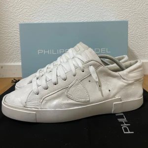Vita sneakers från Philippe Model - Stilrena vita sneakers från Philippe Model med klassisk låg siluett. Skorna är tillverkade i skinn och har rund tå, platt sula och snörning. Perfekta för dig som gillar minimalistisk och clean look. Diskret logga på sidan och snygga detaljer i samma färg. Bra skick, storlek 43! 🙌 Hör av er ifall ni har några frågor! 💬 Nypris runt 3000. Box medföljer.