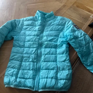 Ljusblå pufferjacka från Hampton Republic - Säljer en ljusblå pufferjacka från Hampton Republic med hög krage och dragkedja framtill. Jackan har ett broderat märke på ena ärmen och quiltad design. Perfekt för kyligare dagar!