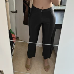 Svarta byxor i skinnimitation - Säljer ett par svarta byxor i skinnimitation från Carin Wester med normal passform och medelhög midja. Byxorna har raka ben och stängs med knapp och dragkedja framtill. Snygga fickor baktill och stilren look som passar till många outfits.