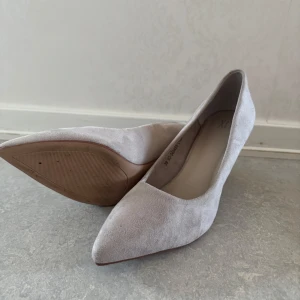 Ljusgrå pumps med spetsig tå - Säljer ett par stilrena ljusgrå pumps med spetsig tå och klack. Skorna är i mocka och har en elegant form som passar perfekt till dig som vill ha en klassisk look.