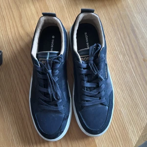 Mörkblå sneakers från Björn Borg - Snygga mörkblå sneakers från Björn Borg med vit sula och klassisk snörning. Skorna har en stilren design med diskreta detaljer och en bekväm passform. Perfekta för dig som gillar en sportig och modern look. Dem har använts 1 gång
