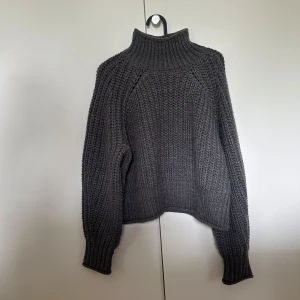 Mörkgrå stickad polotröja - Säljer en chunky mörkgrå stickad polotröja med hög krage. Tröjan har lång ärm och grovstickad struktur som ger en mysig och trendig look. Perfekt för kyliga dagar och enkel att matcha med olika outfits.