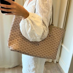 Beige väska  - Säljer en beige väska med klassiskt mönster och matchande liten plånbok. Väskan har två handtag och är rymlig, perfekt för att bära med sig allt man behöver. Ikonisk design med diskret logga och mönster i vitt och brunt.